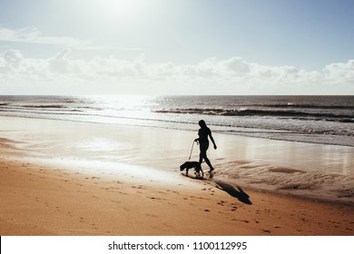 Woman Walking With Dog On Beach At Sunrise