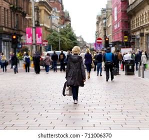 Woman walking down pedestrianised city street towards traffic crossing 
