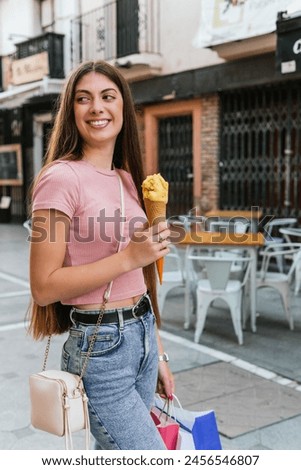 A woman is walking down the street with a cone of ice cream in her hand. She is smiling and she is enjoying her treat. Summer sales concept.