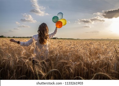 a woman walking int the wheat field holding four color baloon