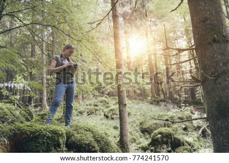Woman walking in a lush forest and taking pictures with a professional digital camera, tourism and adventure concept