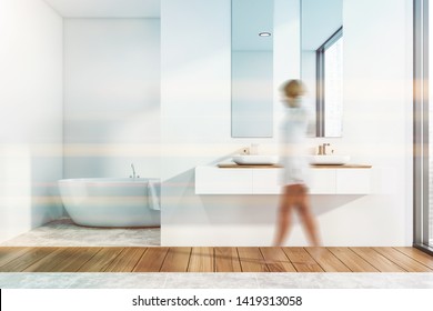 Woman walking in modern bathroom interior with white walls, double sink with mirror and comfortable bathtub in background. Toned image blurred - Powered by Shutterstock