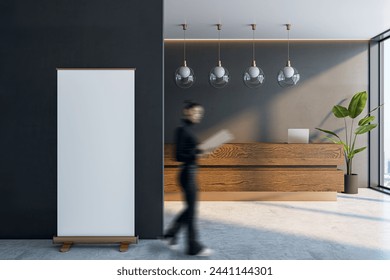 Woman walking in modern office lobby with blank mock up banner on wall, wooden reception desk and concrete walls, window with city view and daylight - Powered by Shutterstock