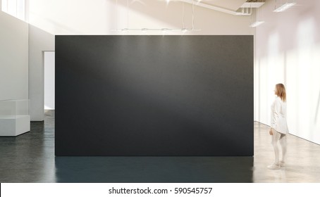 Woman Walking Near Blank Black Wall Mockup In Modern White Gallery. Girl Admires A Dark Big Stand Mock Up In Museum With Contemporary Art Exhibitions. Large Hall Interior, Grey Banner Exposition