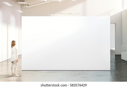 Woman walking near blank white wall mockup in modern gallery. Girl admires a clear big stand mock up in museum with contemporary art exhibitions. Large hall interior, banner exposition