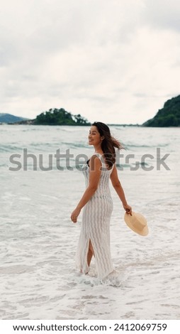 Woman walking in ocean water waves on sandy beach, Female tourist on summer travel vacation, Slow motion, vertical shot
