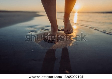 Woman walking on a beach during sunset, close-up of feet.