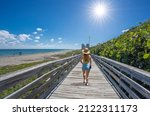 Woman walking on boardwalk on beautiful Florida beach. Girl on summer vacation in Florida. Boardwalk leading to Atlantic Ocean. MacArthur Beach State Park, North Palm Beach, Florida. USA.