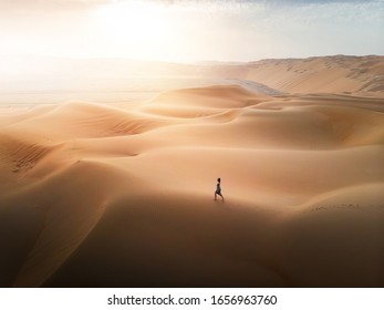 Woman walking on the desert sand dunes aerial view at sunset