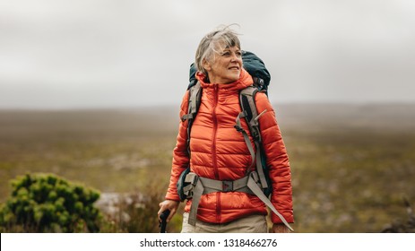 Woman walking on a hill holding a trekking pole. Woman wearing jacket and backpack on a trekking expedition.