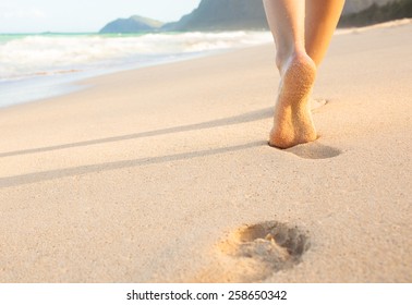 Woman Walking On Sand Beach Leaving Footprints In The Sand.