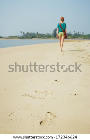 Woman walking on sand beach leaving footprint in the sand.