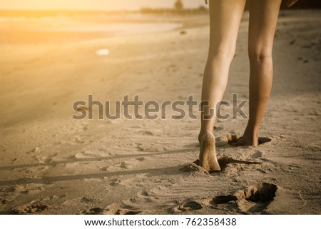 Woman walking on sand beach leaving footprints in the sand.