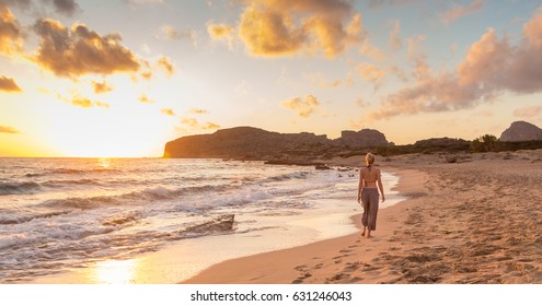 Woman Walking On Sandy Beach At Golden Hour. Seashore Sunset Walk, Falasarna, Crete, Greece.