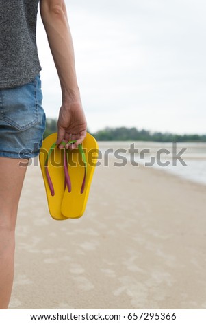 Woman walking on sandy beach with yellow flip flop in hand