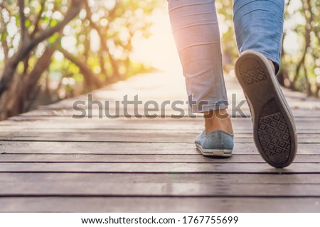 Woman is walking on small wood bridge to nature walk way with sunlight flare background.
