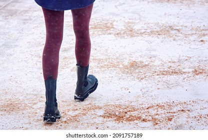 Woman Walking On Snowy Sidewalk Spreading With Sand, Prevention Of Pedestrian Injury. Back View On Female Feet In Winter Black Boots Walking On Snowy And Icy Walkway. Slippery Road Sprinkled With Sand