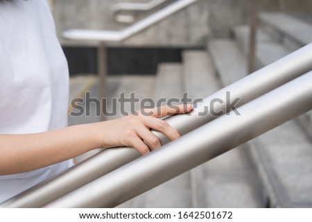 Woman walking on the stair way and grabbing on safety stair rail. Close up shoot on a hand catching a stair rail. Woman aware about safety while walking on the stair way.