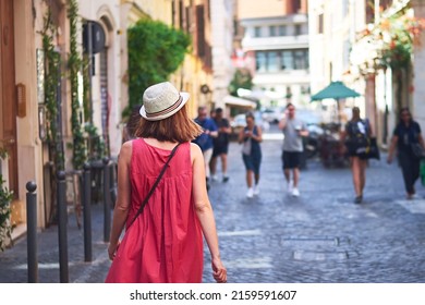 Woman walking on street. Rear view of woman in red dress with hat walking on city street on sunny day. - Powered by Shutterstock