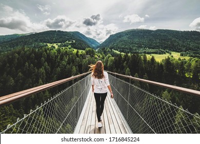 Woman walking on a wooden bridge over a precipice to forests. Switzerland