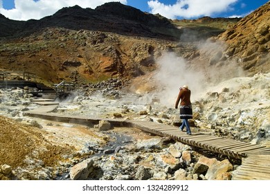 Woman Walking On Wooden Pathway Trying To Breath Through A Sweater Sleeve To Avoid Sulfur Smell - In Krýsuvík / Seltún Geothermal Area In Reykjanes Peninsula In Iceland. 