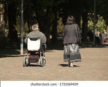 A woman is walking in the park with a man who is traveling on an electric wheelchair. Custody of the needy. The activity of people with limited mobility. Prosthetics of patients of the musculoskeletal - Powered by Shutterstock