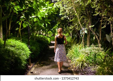 Woman Walking In A Park With Tropical Trees At Night