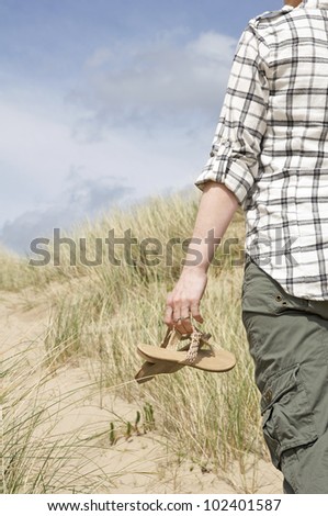 woman walking in sand dunes holding sandals on a sunny day