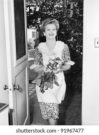 Woman Walking Through A Doorway With Flowers In Her Hands