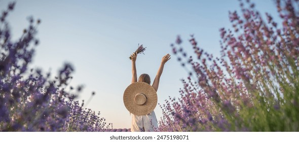 A woman is walking through a field of purple flowers with a straw hat on - Powered by Shutterstock