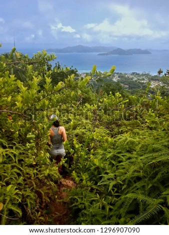 Woman walking through green branches. Scenic view of island of praslin and ocean.