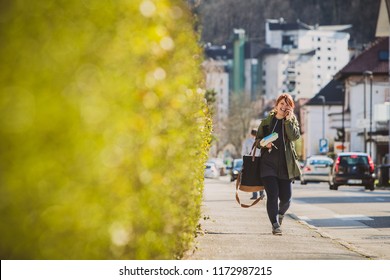Woman Walking Towards The Camera Smiling, Talking On The Telephone And Carrying Full Load Of Bags, Eggs And Car Keys. Woman In Suburban Environmet In Europe Carrying Too Much Stuff.