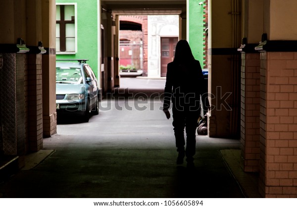 Woman walking in a tunnel passage to the parking\
area of an apartment\
complex.