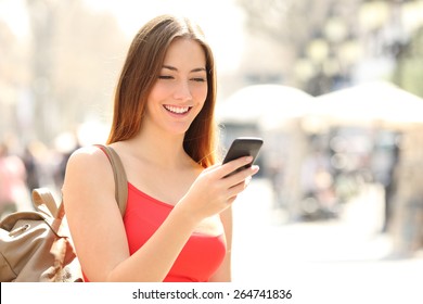Woman walking and using a smart phone in the street in a sunny summer day