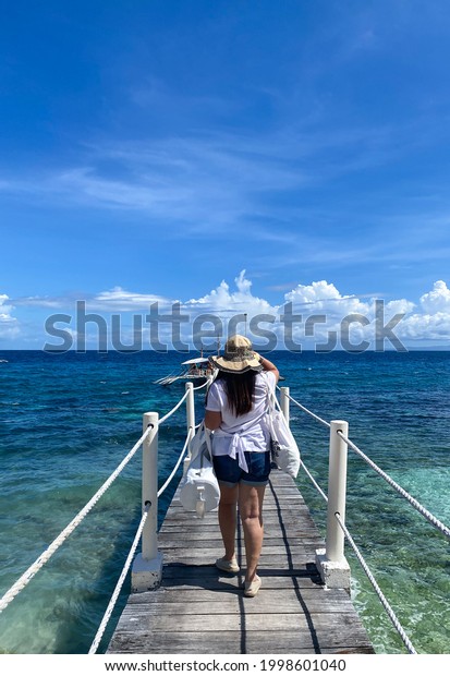 A\
woman walking in a wooden pier towards a waiting\
boat.