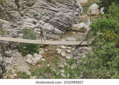 A woman walks across a suspension bridge over a rocky stream in Goynuk Canyon, surrounded by rugged nature. Ideal for promoting eco-tourism, hiking, and outdoor adventure travel experiences.  - Powered by Shutterstock