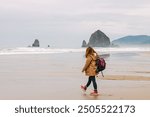 A woman walks along the serene beach at Cannon Beach, Oregon, exploring the coastline on a cloudy day