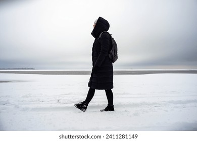 A woman walks along a snowy winter river bank - Powered by Shutterstock