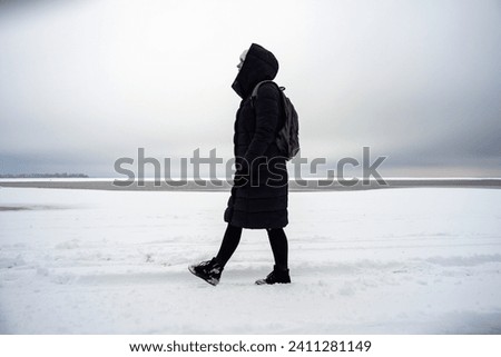 A woman walks along a snowy winter river bank