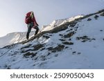 woman walks with a backpack in the middle of a mountainous landscape with snowy peaks in the background of the landscape and carrying technical mountaineering and climbing equipment with style 