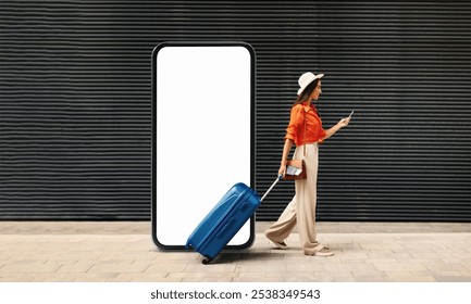 A woman walks with a blue suitcase while checking her smartphone, standing next to a large blank display. This urban setting suggests a busy travel hub during the day.