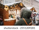 Woman walks to Christmas market during the Advent holiday. Snowing in city at winter. Festive fair in xmas