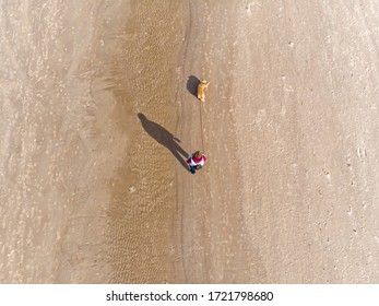 A Woman Walks With A Dog Along The Sand Dunes Along The Sea Shore, View From Above