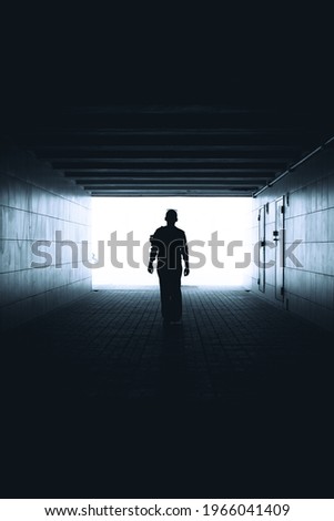 The woman walks down the tunnel towards the light. Silhouette of a woman walking in the underpass