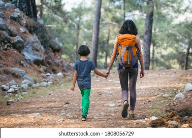 A Woman Walks With Her Son Through The Forest. The Boy With His Mother Go Hiking. A Child With A Backpack Is In The Park. Travel With Children. The Kid Holds Mom's Hand. Mountain Trail.