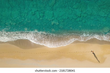 Woman walks on the beach along breaking waves leaving footprints on a sand. Aerial view directly above - Shutterstock ID 2181728041