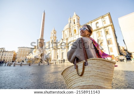 Woman walks on Navona square in Rome city on a sunny day. Female person with bag and colorful shawl in hair. Concept of italian lifestyle and travel