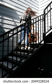 Woman Walks Up Stairs In Leather Jacket, Carrying A Weekender Bag