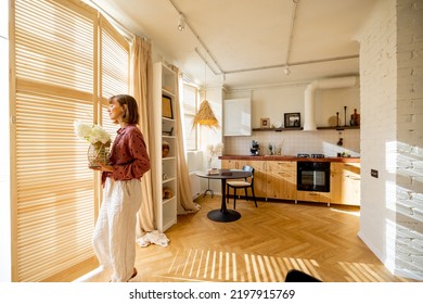 Woman Walks With A Vase Of Flowers, Decoration And Having Some House Chores At Home. Wide Interior View On Sunny Studio Apartment In Beige Tones