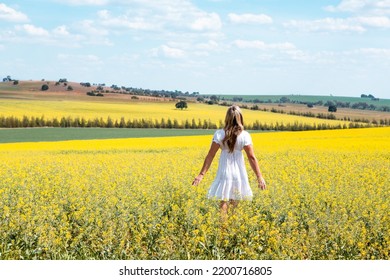 Woman Wanders In Fields Of Flowers.  She Is Wearing A Simple White Cotton Dress